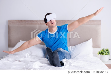 Young man in bed wearing a vr virtual reality head set Young man in bed wearing a vr virtual reality head set 61038587