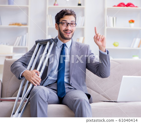 Businessman with crutches and broken leg at home working 61040414