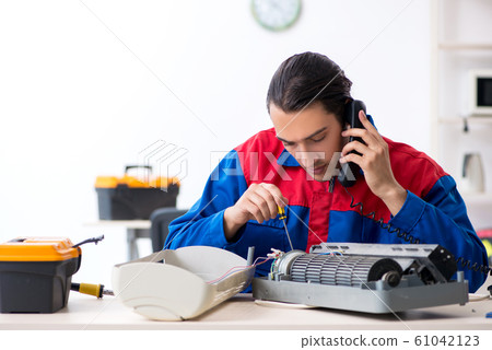Young repairman repairing air-conditioner at warranty center Young repairman repairing air-conditioner at warranty center 61042123