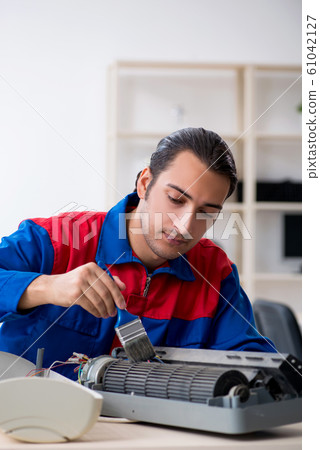 Young repairman repairing air-conditioner at warranty center Young repairman repairing air-conditioner at warranty center 61042127