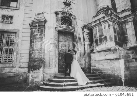 Wedding photo shooting. Bride and bridegroom walking in the city. Married couple embracing and looking at each other. Holding bouquet 61043691