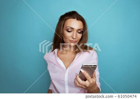 Pretty brunette using phone in the blue studio. 61050474