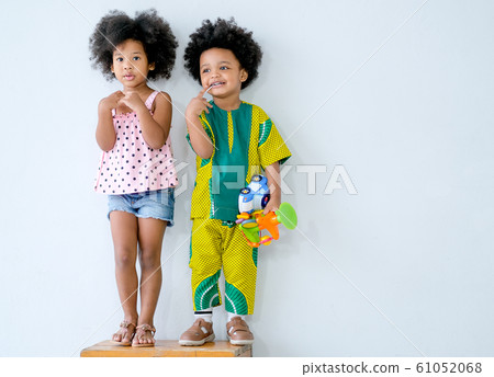 Two young African little boy and girl stand in front of white wall and express different action 61052068