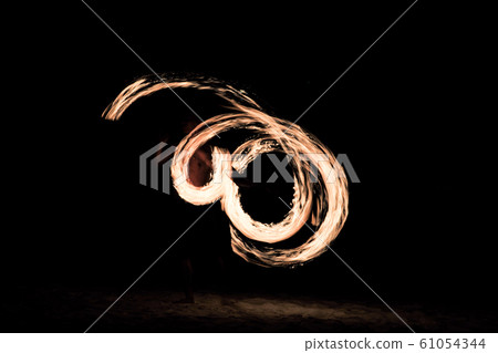 Motion blurred portrait of man dances with fire on the beach with dark night background 61054344