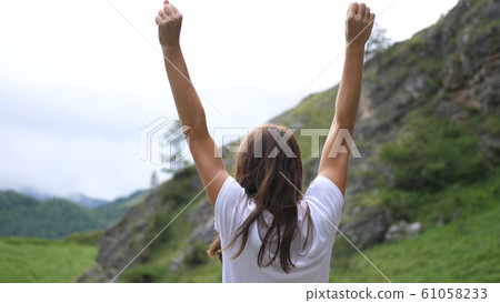Successful young woman standing on the top of the mountain raises her hands up. Back of view 61058233