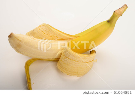 One ripe yellow partially peeled banana on a white 61064891