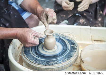The potter makes pottery dishes on potter's wheel. 61069822