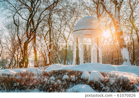 Gomel, Belarus. Winter City Park. Sun at sunset shining through gazebo in city park. Garden pergola in snow Gomel, Belarus. Winter City Park. Sun at sunset shining through gazebo in city park. Garden pergola in snow 61070826