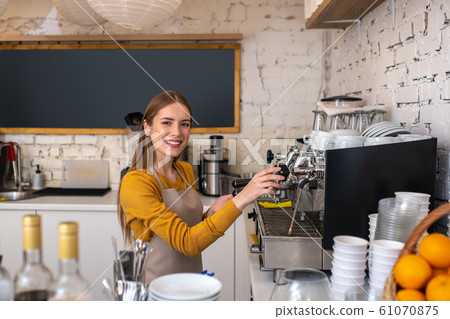 Smiling young barista using espresso coffee machine 61070875