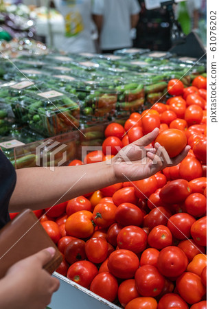 Woman holding purse and picking perfect tomato at grocery store Woman holding purse and picking perfect tomato at grocery store 61076202