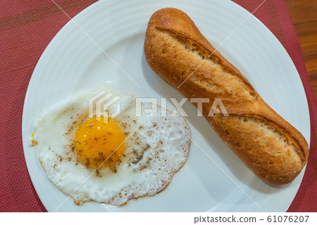 Baguette bread and sunny egg on white plate for breakfast 61076207