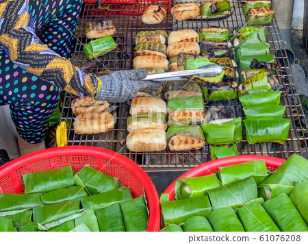 Woman grilling sticky rice banana at Cambodia outdoor market 61076208