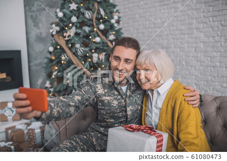 Smiling man in camouflage uniform making selfie with mom 61080473