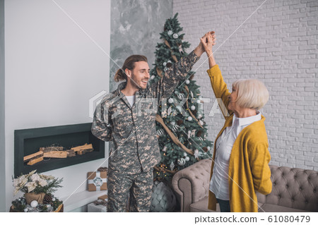 Handsome man in camouflage dancing with mom near christmas tree Handsome man in camouflage dancing with mom near christmas tree 61080479