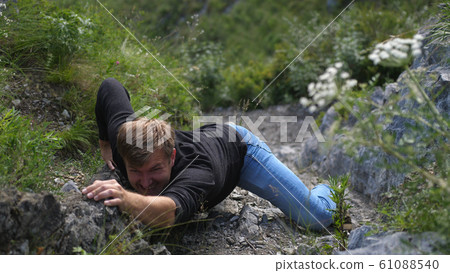 A man hardly climbs on a rock reached the top of the cliff A man hardly climbs on a rock reached the top of the cliff 61088540