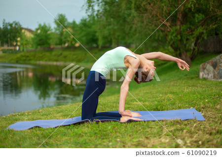 A young sports girl practices yoga on a green lawn A young sports girl practices yoga on a green lawn 61090219