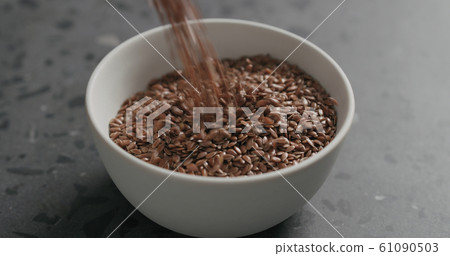 closeup flaxseed falling into white bowl on terrazzo countertop 61090503