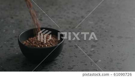 flaxseed falling into black bowl on terrazzo countertop 61090726