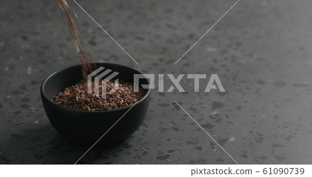 flaxseed falling into black bowl on terrazzo countertop 61090739