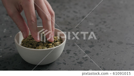 man hand takes pumpkin seeds from white bowl with copy space man hand takes pumpkin seeds from white bowl with copy space 61091015