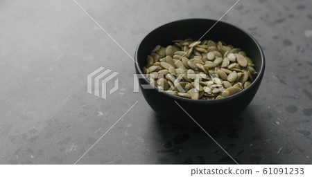 pumpkin seeds in black bowl on terrazzo countertop with copy space 61091233