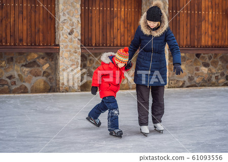 young mother teaching her little son ice skating at outdoor skating rink. Family enjoy winter on ice young mother teaching her little son ice skating at outdoor skating rink. Family enjoy winter on ice 61093556