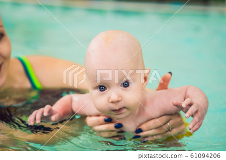 Beautiful mother teaching cute baby girl how to swim in a swimming pool. Child having fun in water 61094206