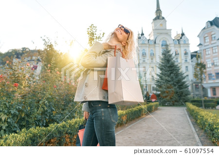 Young smiling blonde woman with curly hair with bags for shopping, sunny city background, golden hour 61097554
