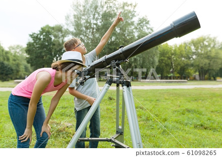 Children teenagers in the park looking through a telescope 61098265