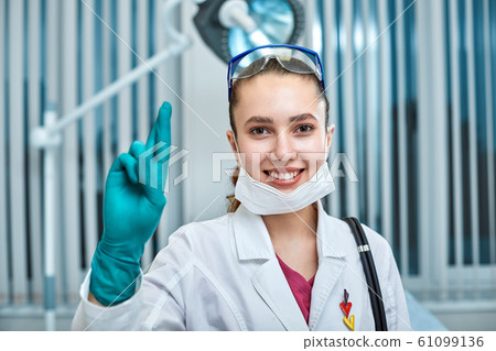 young beautiful woman doctor in white uniform and mask on her face close up on clinic background 61099136