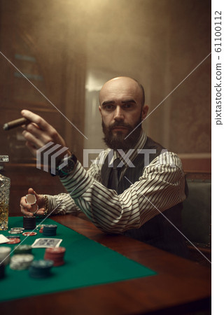 Bearded poker player with cigar playing in casino 61100112