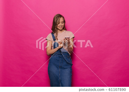 Cheerful young woman using mobile phone on isolated pink background. Cheerful young woman using mobile phone on isolated pink background. 61107890