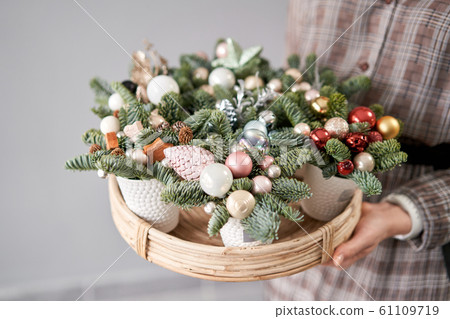 Florist holds a tray with christmas arrangements. Beautiful festive arrangement of fresh spruce in coffee Cup. Christmas mood. Florist holds a tray with christmas arrangements. Beautiful festive arrangement of fresh spruce in coffee Cup. Christmas mood. 61109719
