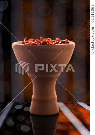 Shisha in a clay bowl stands against a fabulous bokeh with diagonal lines on a glossy surface with reflections. Traditions of hookah Smoking. Shisha in a clay bowl stands against a fabulous bokeh with diagonal lines on a glossy surface with reflections. Traditions of hookah Smoking. 61111068