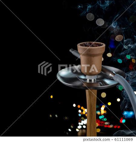 Clay bowl with Shisha on a modern Smoking hookah with oak fragments on a beautiful dark background with colored bokeh. Clay bowl with Shisha on a modern Smoking hookah with oak fragments on a beautiful dark background with colored bokeh. 61111069