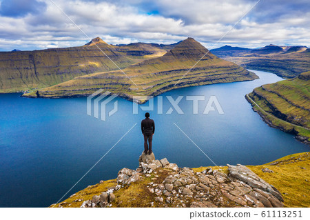 Hiker enjoys views over fjords from a mountain near Funningur on Faroe Islands 61113251