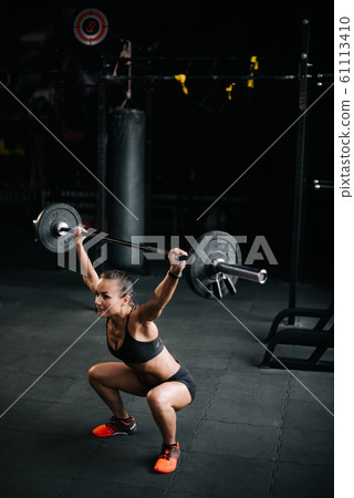 Sporty woman bodybuilder lifts heavy barbell over her head. Sporty woman bodybuilder lifts heavy barbell over her head. 61113410