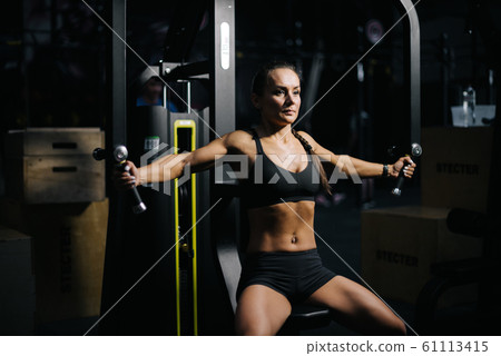 Strong muscular woman with perfect fitness body works out on gym equipment 61113415