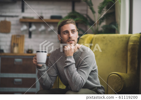 Young bearded handsome man with cup sitting in armchair Young bearded handsome man with cup sitting in armchair 61119200