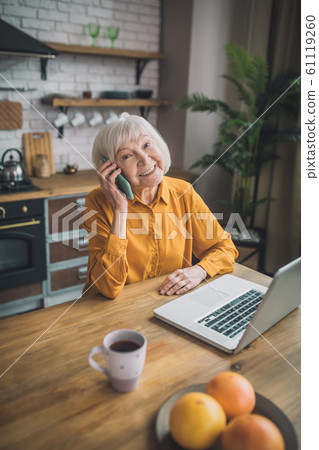Good-looking elderly lady in yellow talking on the phone 61119260