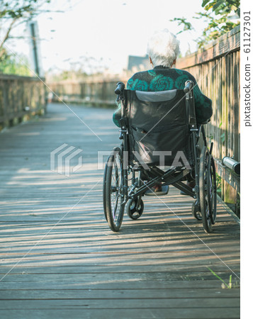 Picture of lonely old woman sitting on the wheelchair while looking at sunlight. 61127301
