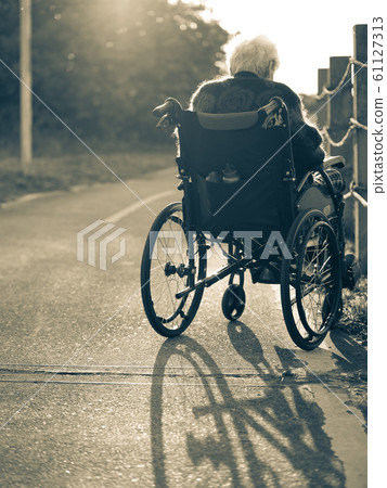 Picture of lonely old woman sitting on the wheelchair while looking at sunlight. Picture of lonely old woman sitting on the wheelchair while looking at sunlight. 61127313