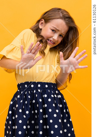 girl in a t-shirt and skirt waving her arms in displeasure and denies on a yellow background 61130126