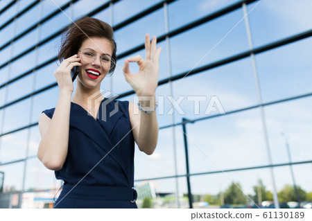 business lady girl in a sleeveless suit shows the class and talking on the phone against the 61130189