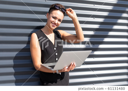 attractive charming business woman with a laptop in her hands stands against the background wall of 61131480