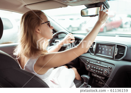 A woman driving a car, looking in the rearview mirror, reversing, parking at a shopping center, driving a car into the garage. Summer girl in a dress. Automatic transmission. Vehicle interior. 61136159