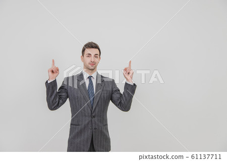 Successful handsome businessman standing, presenting a project, pointing his fingers up, smiling. 61137711