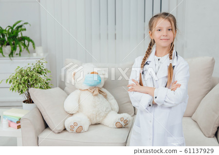 Pretty confident little girl wearing doctor coat, stethoscope standing, folding her hands, looking at the camera. Pretty confident little girl wearing doctor coat, stethoscope standing, folding her hands, looking at the camera. 61137929