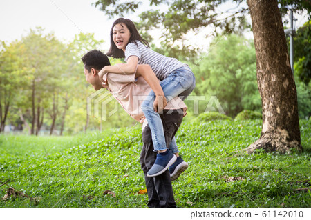 Happy asian father laugh giving piggyback ride to beautiful daughter having fun,hug together,smiling child girl enjoying active game with dad, young man carrying cute daughter on back,playing in outdo 61142010