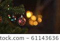 a glass toy hangs on a decorated Christmas tree, against the background of flashing lights and a burning fireplace. 61143636